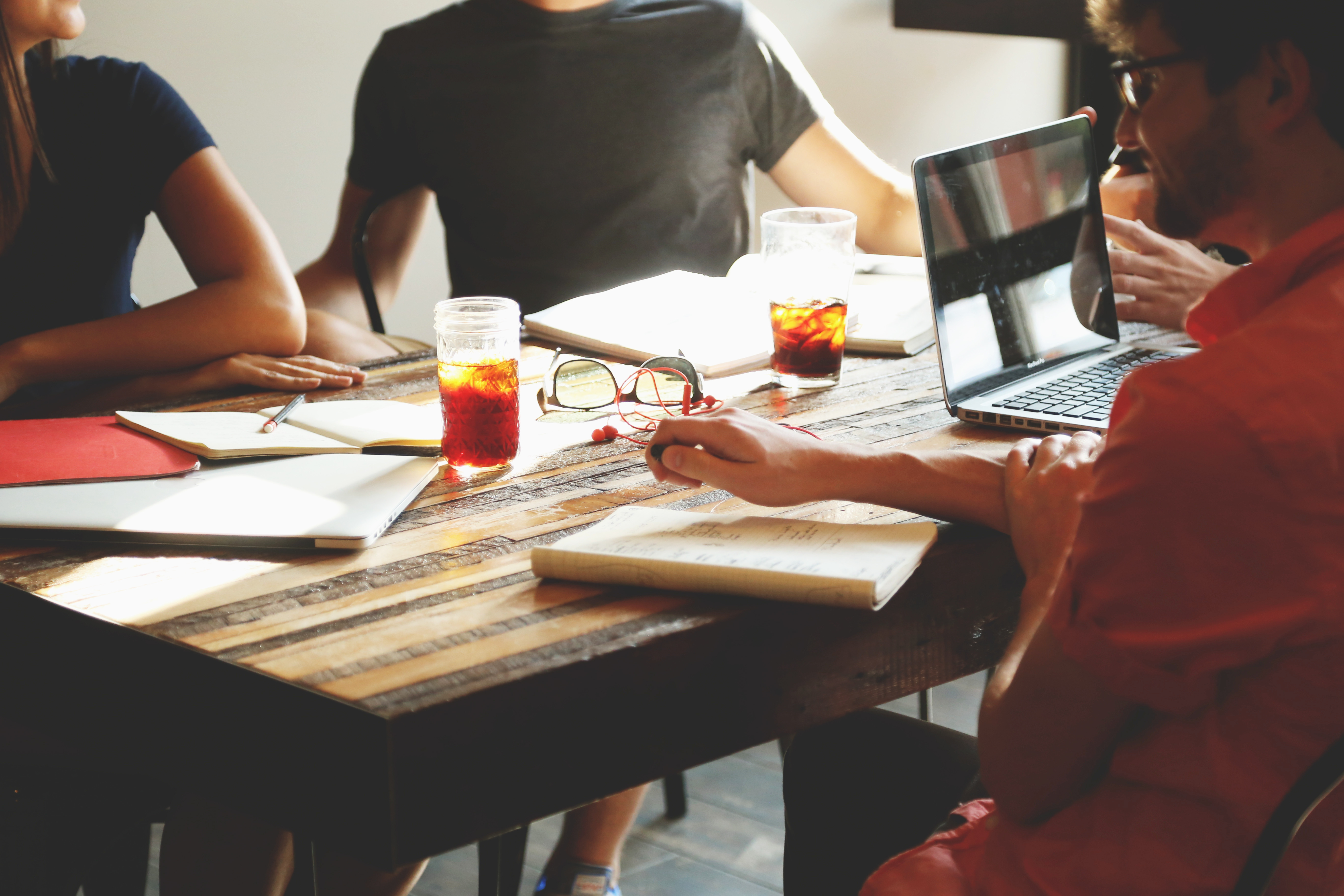 Drei Personen sitzen zu einer Besprechung des Themas Digital Asset Management am Tisch mit Getränken und Notizblöcken